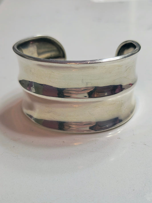 Front view of solid sterling silver horizon-band cuff bracelet with smooth, minimal profile, open-ended and slightly oval-shaped, on a light background.