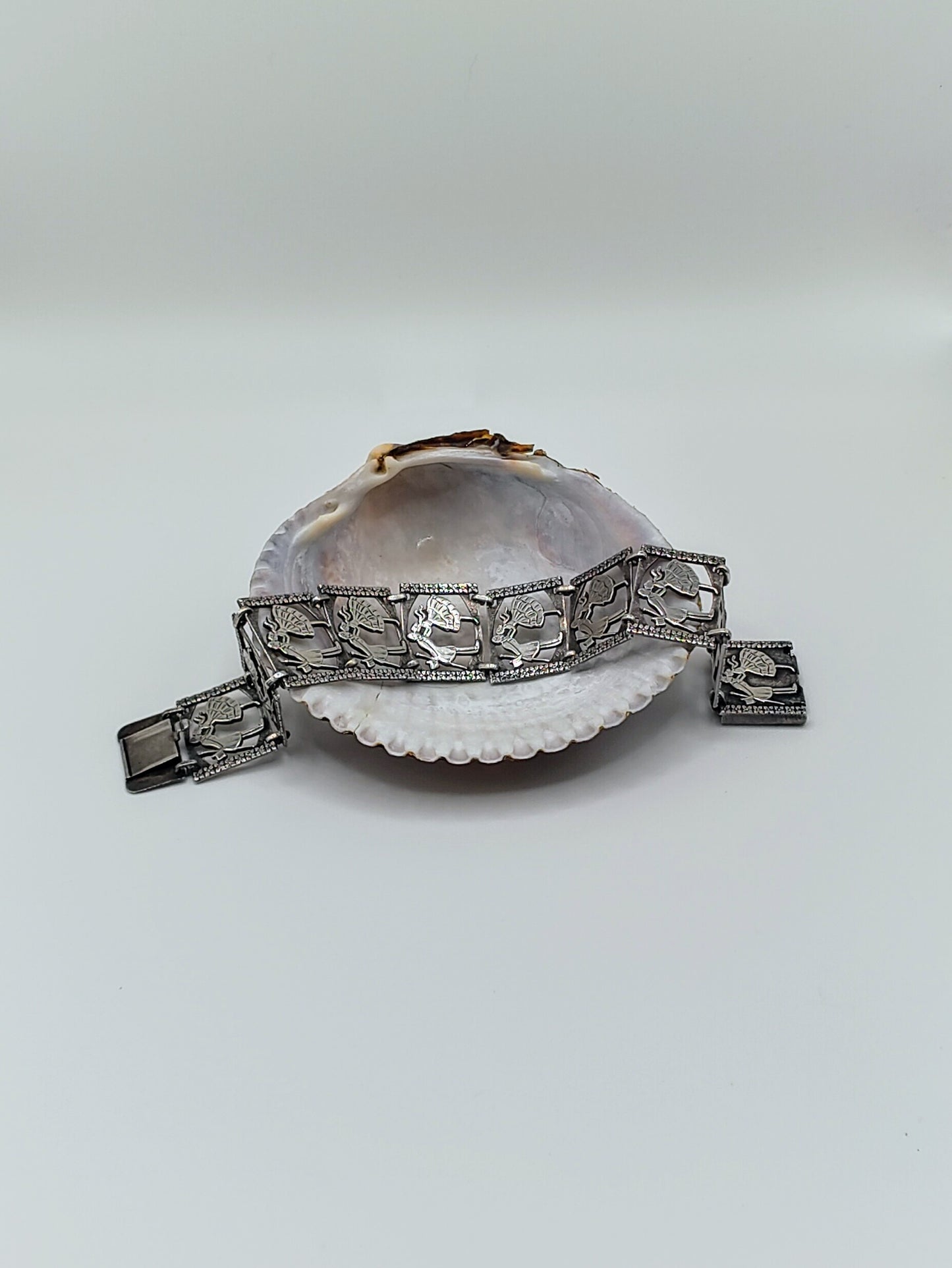 Sterling silver panel bracelet with raised dancing couple designs draped across a white seashell on a light background.