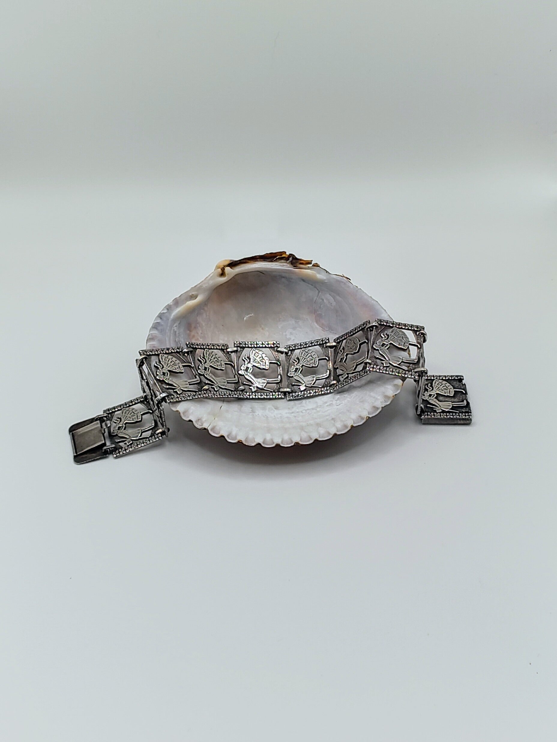 Sterling silver panel bracelet with raised dancing couple designs draped across a white seashell on a light background.