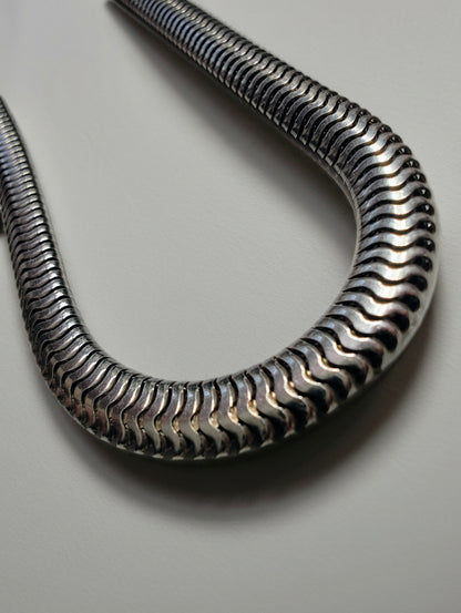 Heavy sterling silver snake chain necklace strung out on a white background, showing its tight, wave-like links.
