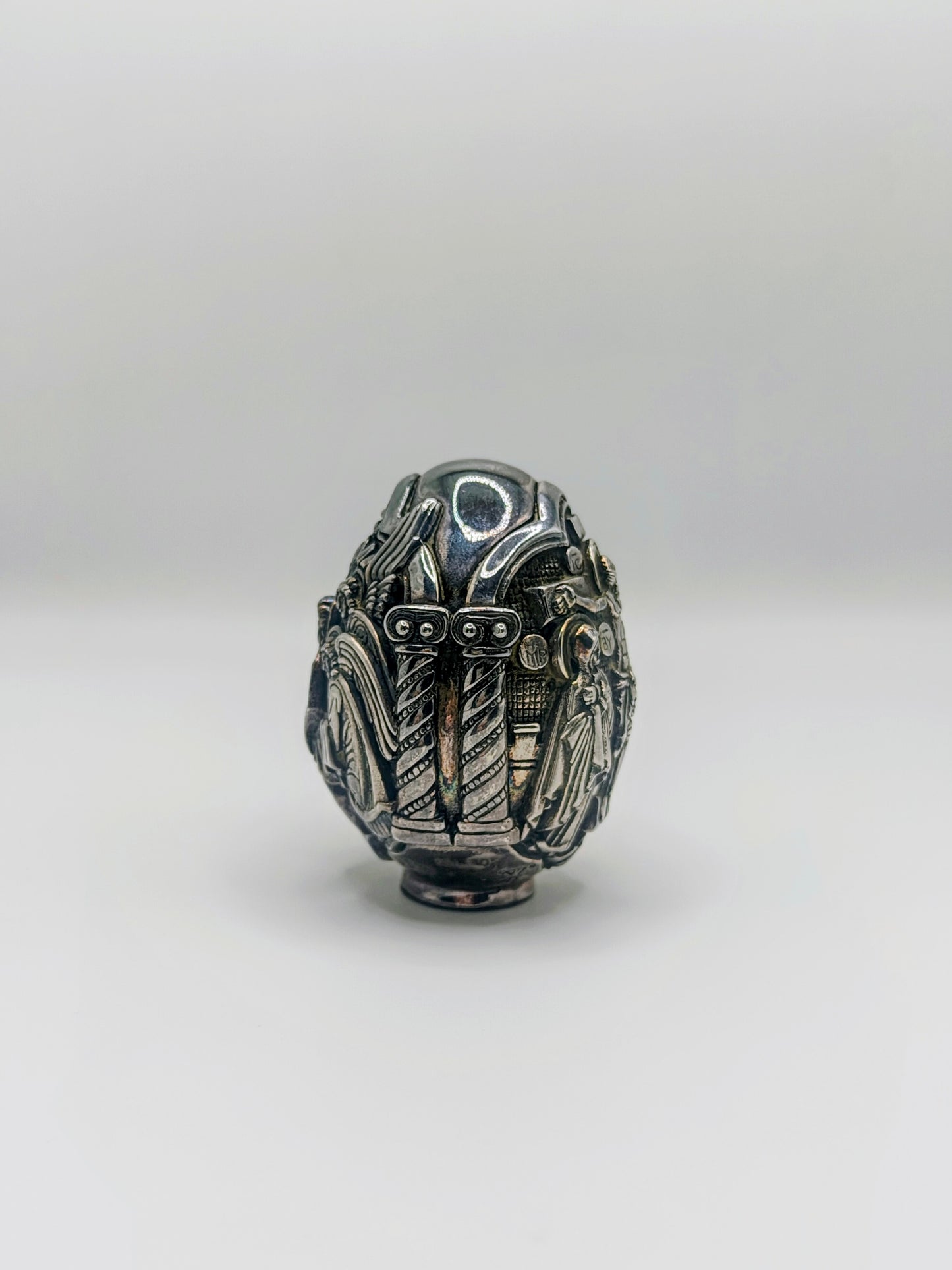 Palm-sized fine silver egg from Greece, richly carved with raised religious icon scenes and darkened recesses.