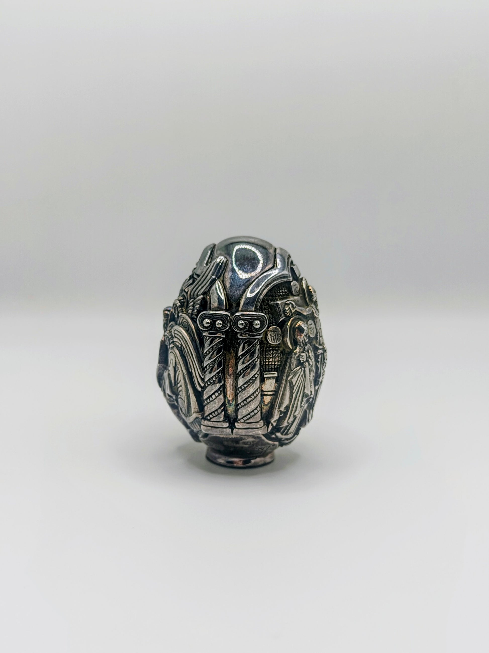 Palm-sized fine silver egg from Greece, richly carved with raised religious icon scenes and darkened recesses.