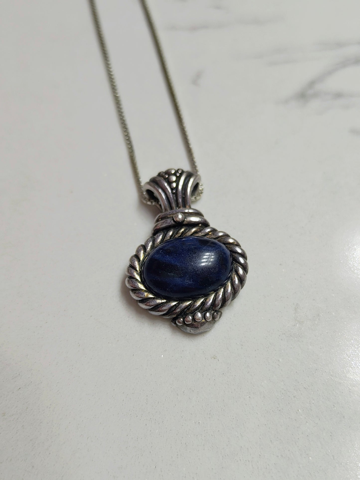 Sodalite Wisdom Necklace lying flat on a light surface, highlighting the blue stone and detailed sterling silver setting.