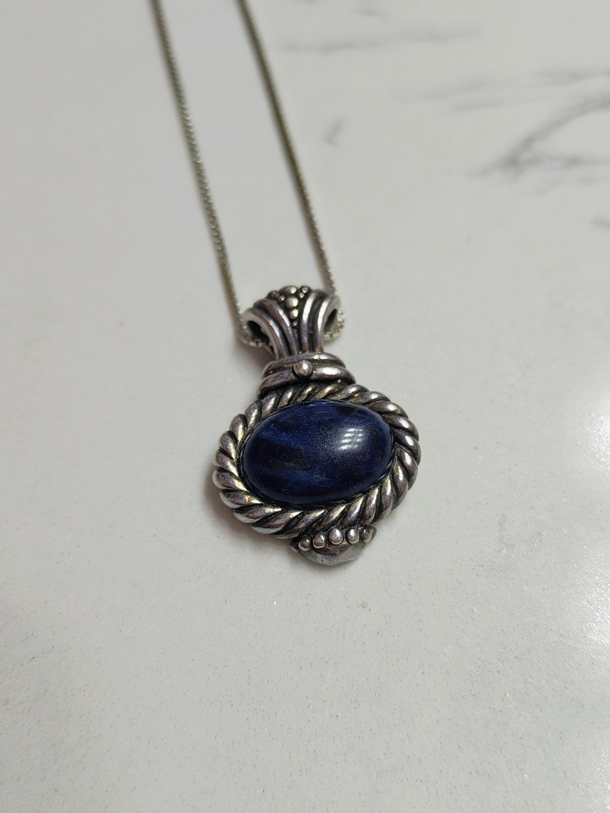 Sodalite Wisdom Necklace lying flat on a light surface, highlighting the blue stone and detailed sterling silver setting.