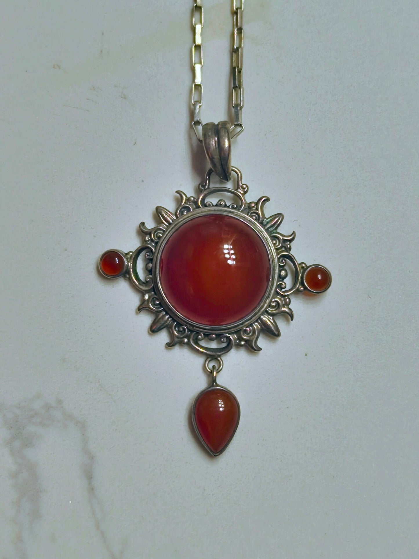 Sterling silver pendant necklace with a domed carnelian stone, two small side carnelian cabochons, and a dangling teardrop