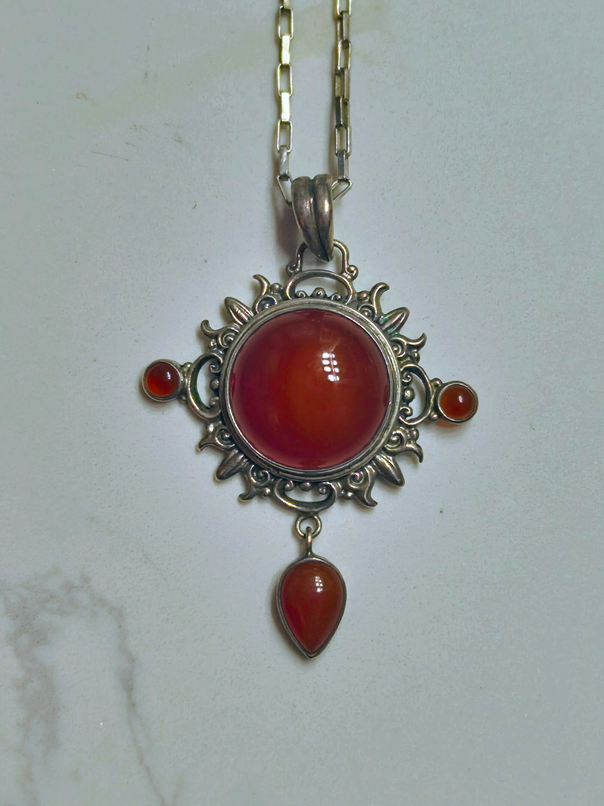 Sterling silver pendant necklace with a domed carnelian stone, two small side carnelian cabochons, and a dangling teardrop