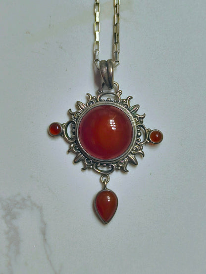 Sterling silver pendant necklace with a domed carnelian stone, two small side carnelian cabochons, and a dangling teardrop