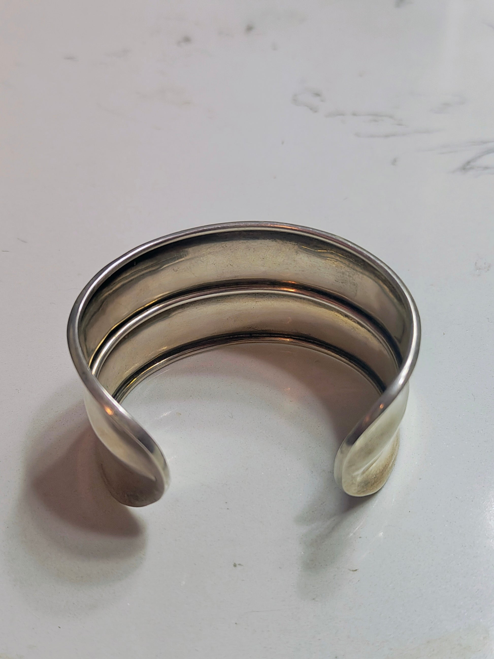 Back view of solid sterling silver horizon-band cuff bracelet with minimal profile, open-ended and slightly oval-shaped.