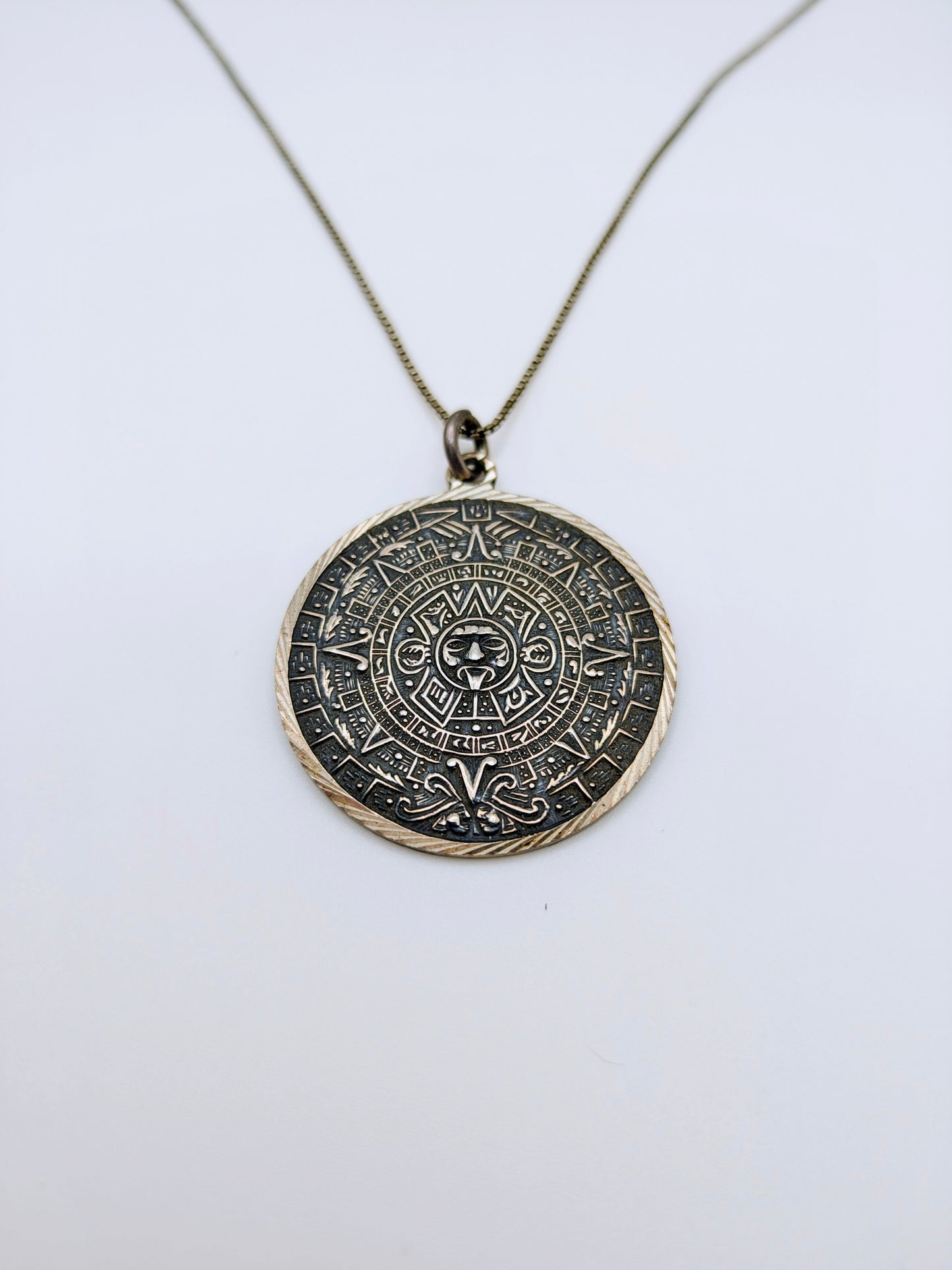 Round sterling silver pendant carved with a detailed Mesoamerican Sun Stone calendar design, oxidized for contrast.