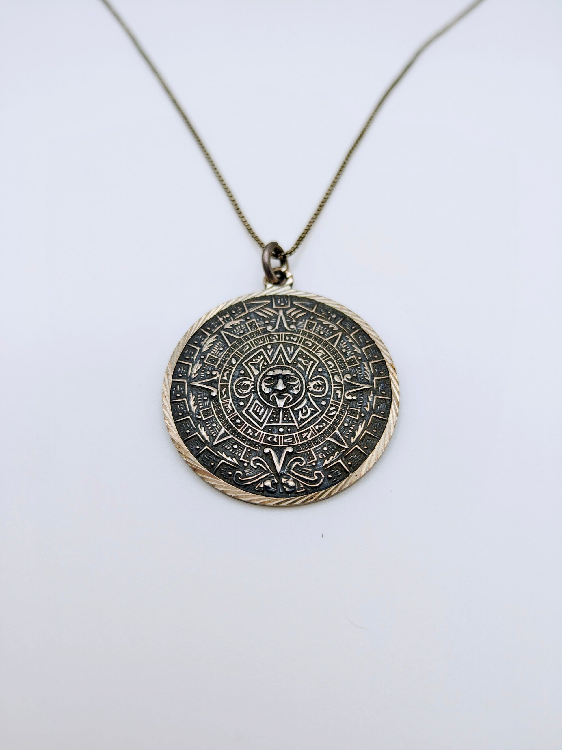 Round sterling silver pendant carved with a detailed Mesoamerican Sun Stone calendar design, oxidized for contrast.