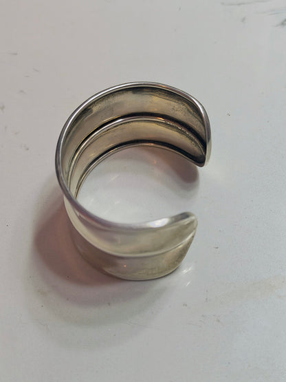 Side view of solid sterling silver horizon-band cuff bracelet with minimal profile, open-ended and slightly oval-shaped.