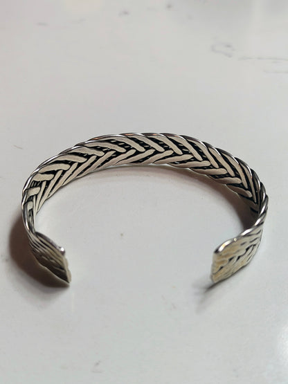 Sterling silver braided cuff bracelet with oxidized recessed pattern and polished raised strands, open-ended and oval-shaped.