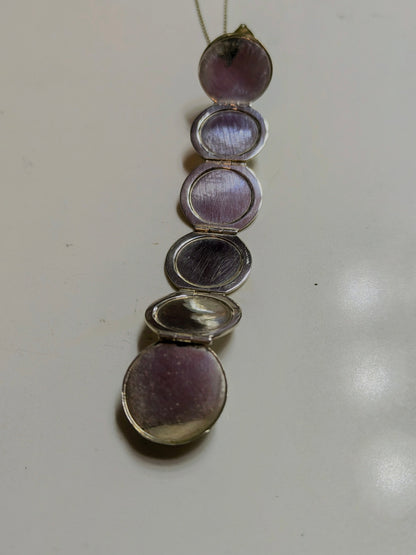 World Within sterling silver orb locket unfolded into six small crescent compartments, laid out on a light surface with chain