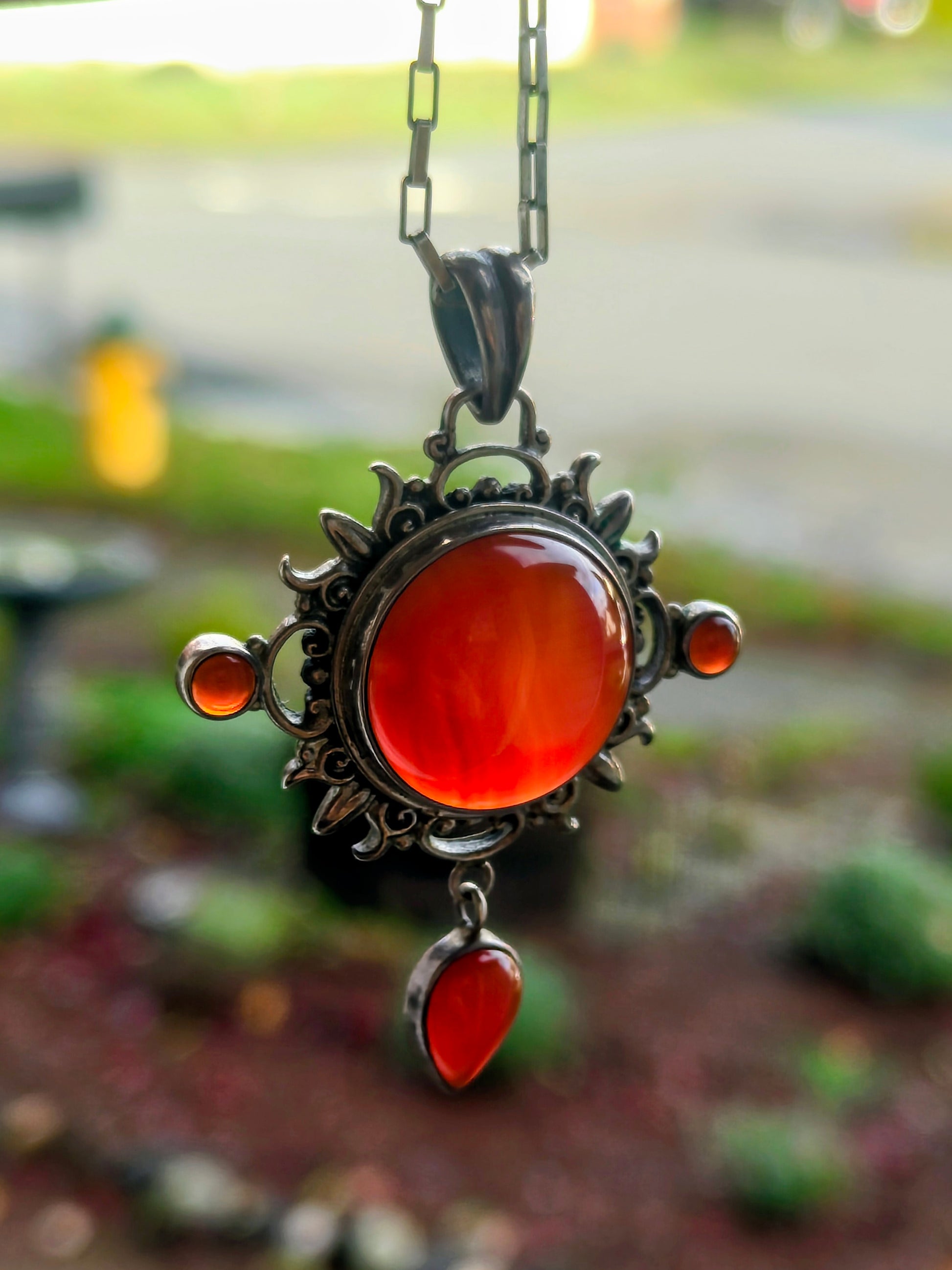 Carnelian Keeper Necklace hanging from a silver chain, glowing orange-red carnelian stones.