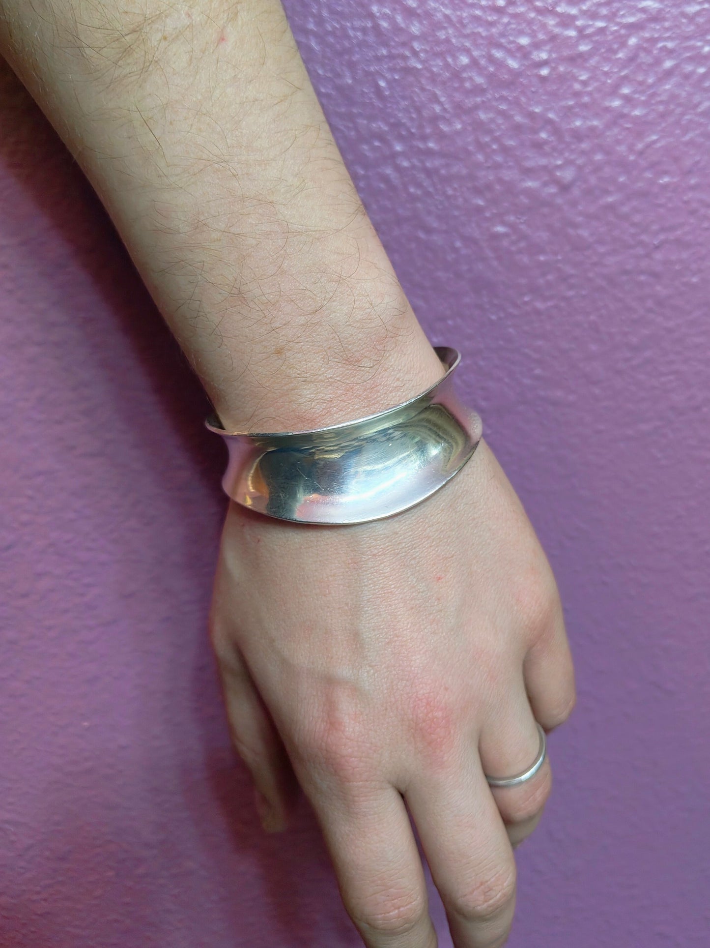 Lunar Flow Bone Cuff worn on a wrist, showing the wide curved sterling silver band against a purple wall.