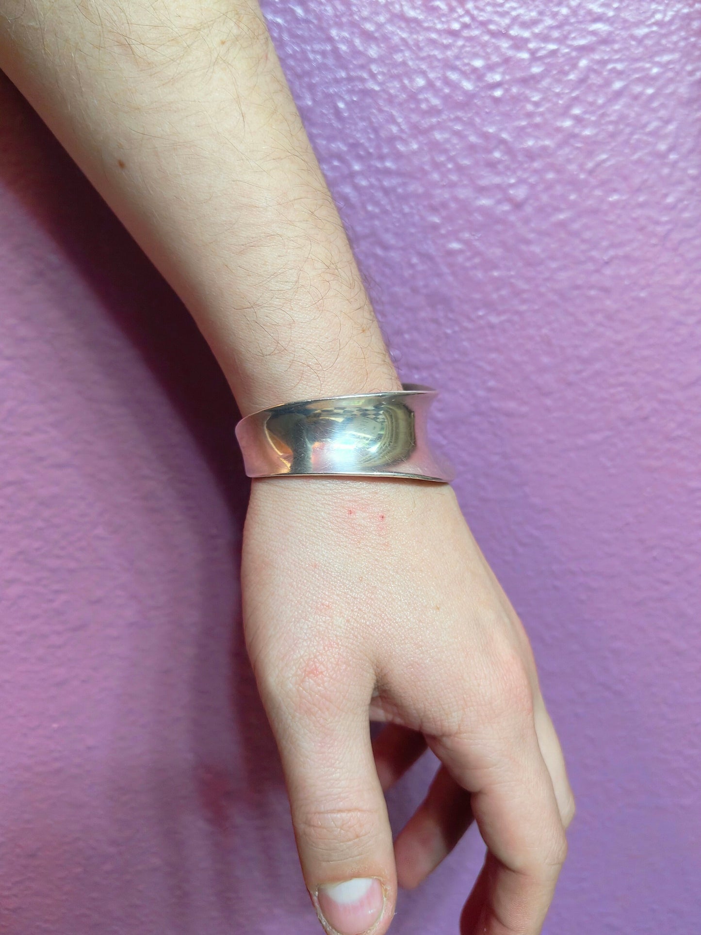 Lunar Flow Bone Cuff worn on a wrist, showing the wide curved sterling silver band against a purple wall.