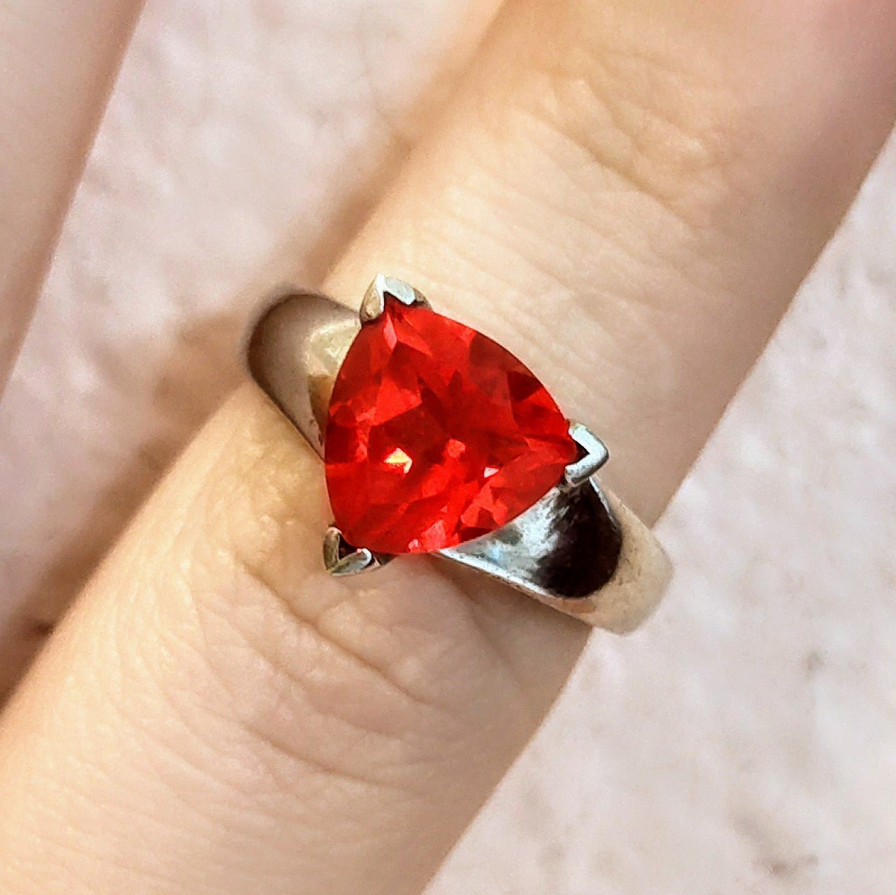 Sterling silver ring featuring a bright triangular-cut red spinel gemstone, displayed on a finger with pink background.