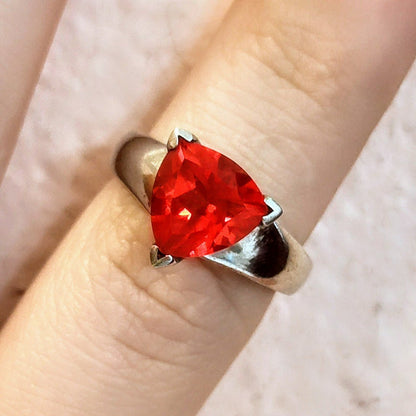 Sterling silver ring featuring a bright triangular-cut red spinel gemstone, displayed on a finger with pink background.