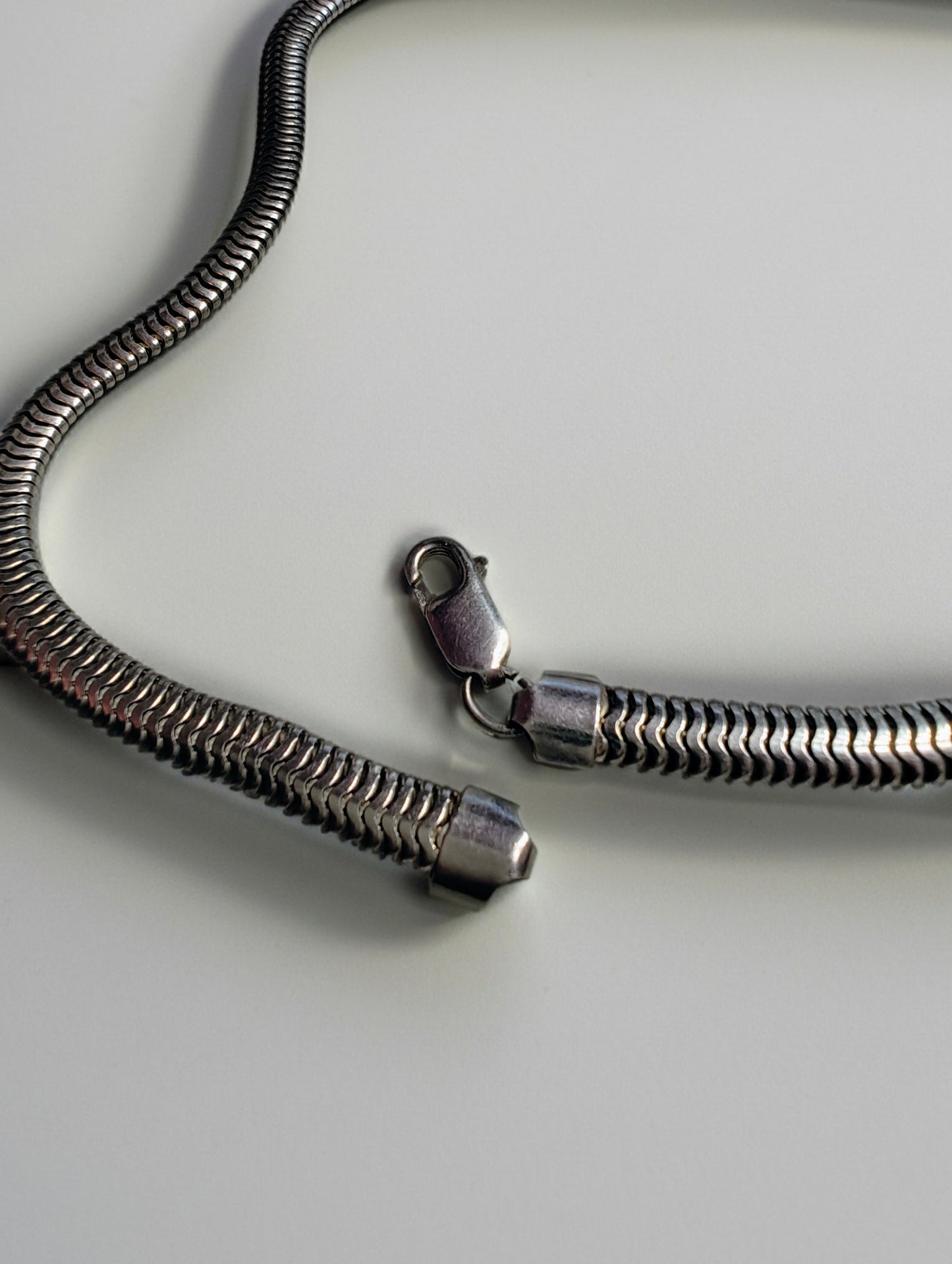 Heavy sterling silver snake chain necklace strung out on a white background, showing its tight, wave-like links and clasp.