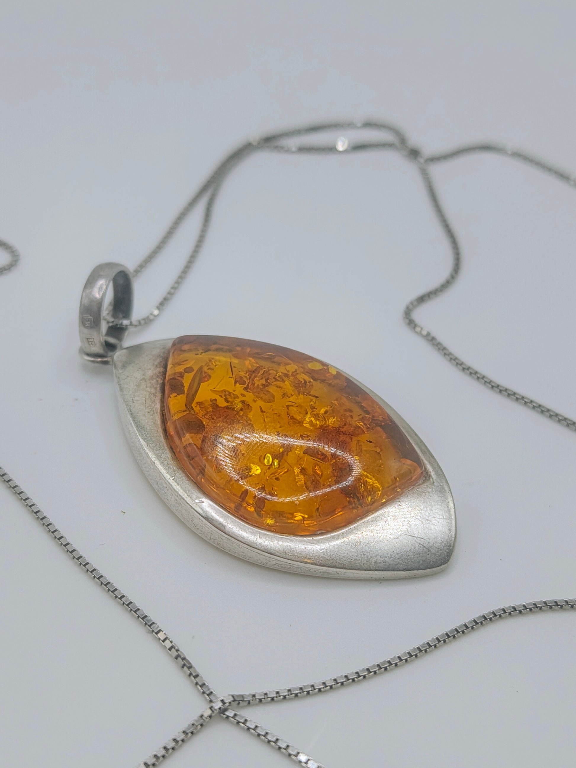 Close-up of a marquise-shaped golden amber pendant in a smooth sterling silver bezel on a silver chain.