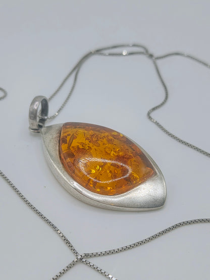 Close-up of a marquise-shaped golden amber pendant in a smooth sterling silver bezel on a silver chain.