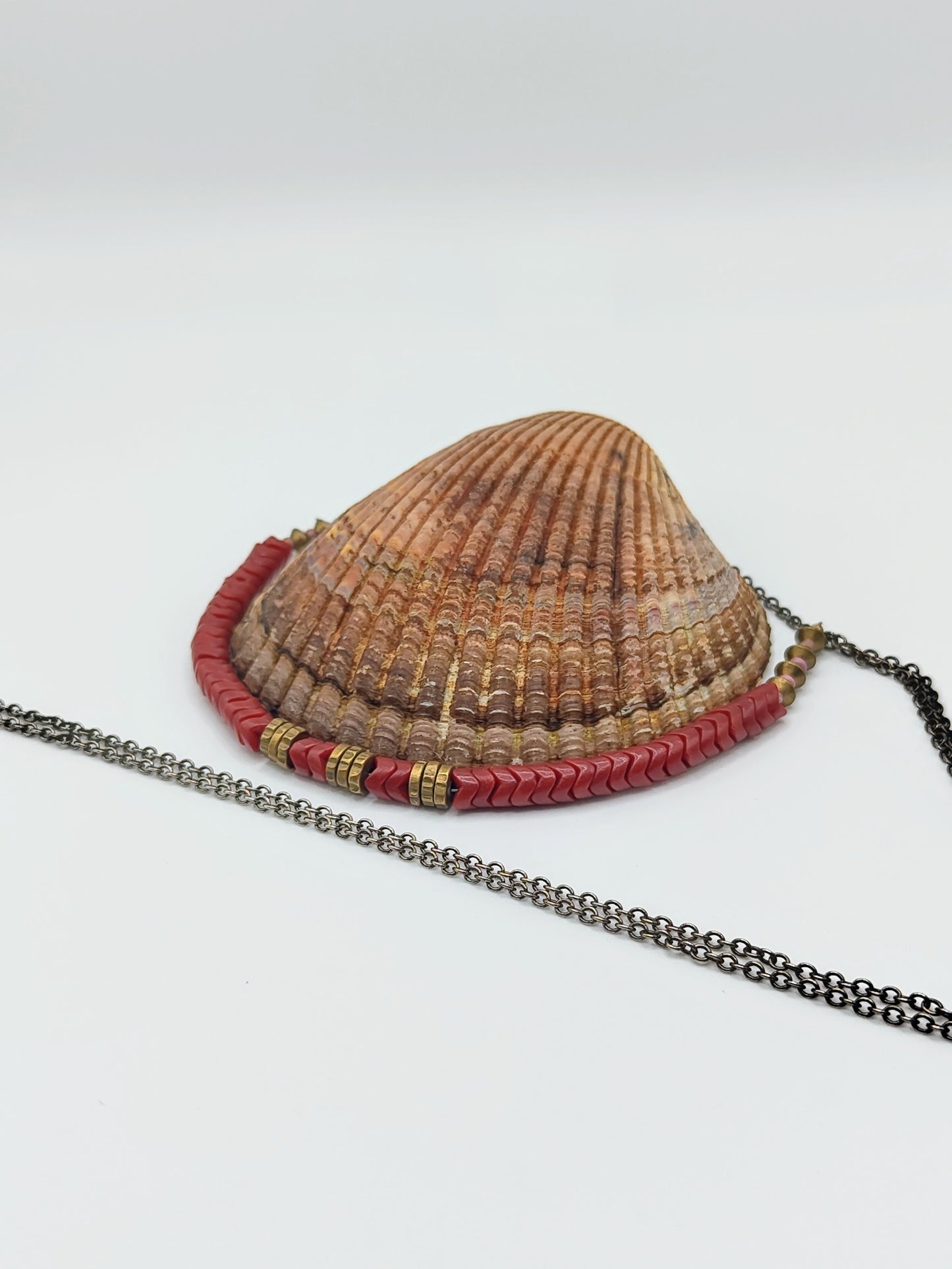 Long mixed-metal necklace with coral-red chevron beads and brass spacers on an oxidized silver chain