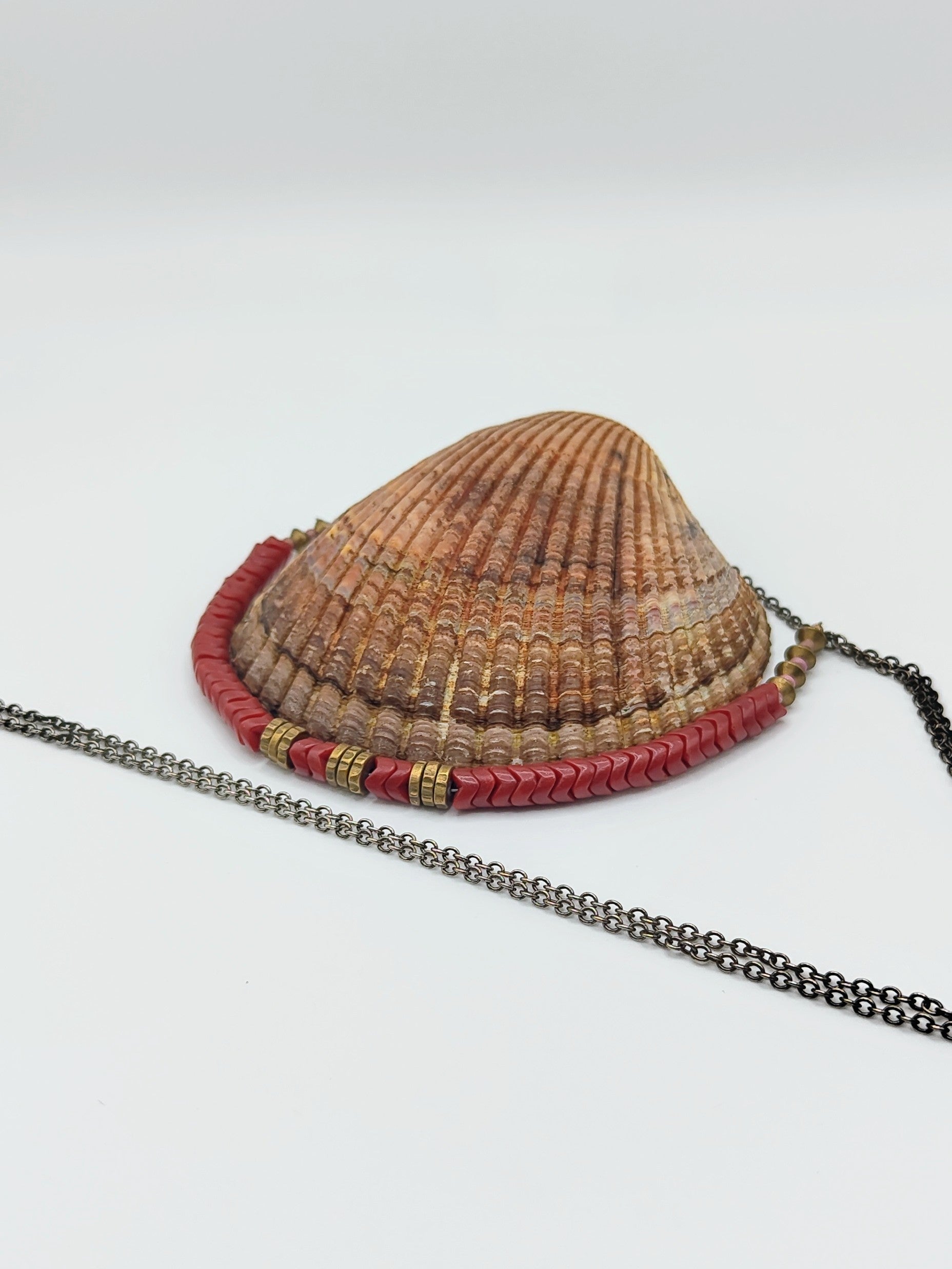 Long mixed-metal necklace with coral-red chevron beads and brass spacers on an oxidized silver chain