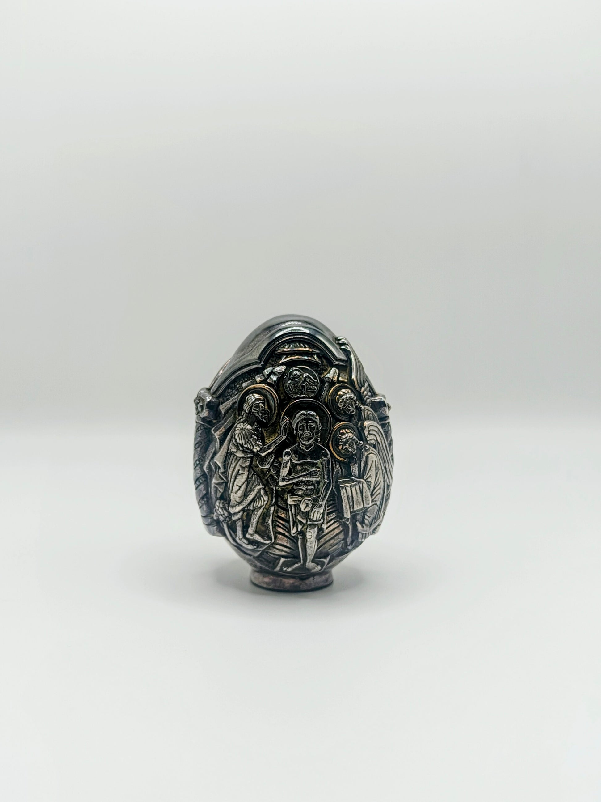 Palm-sized fine silver egg from Greece, richly carved with raised religious icon scenes and darkened recesses.
